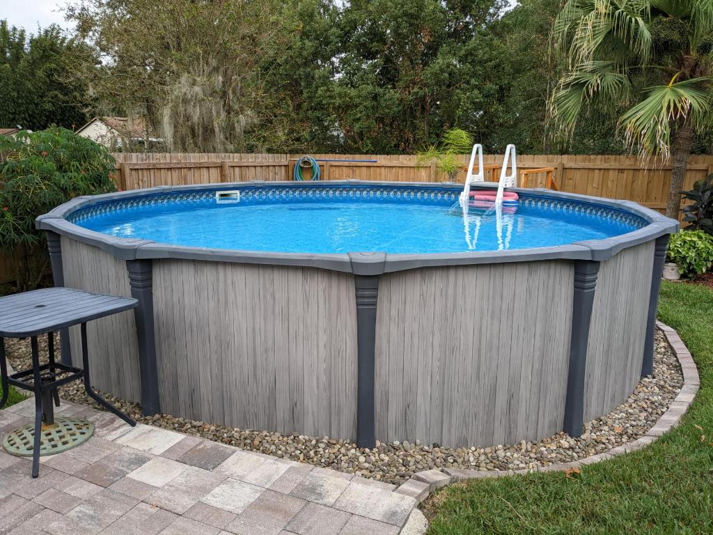 18' above ground swimming pool bordered with rocks and having a deck made with pavers
