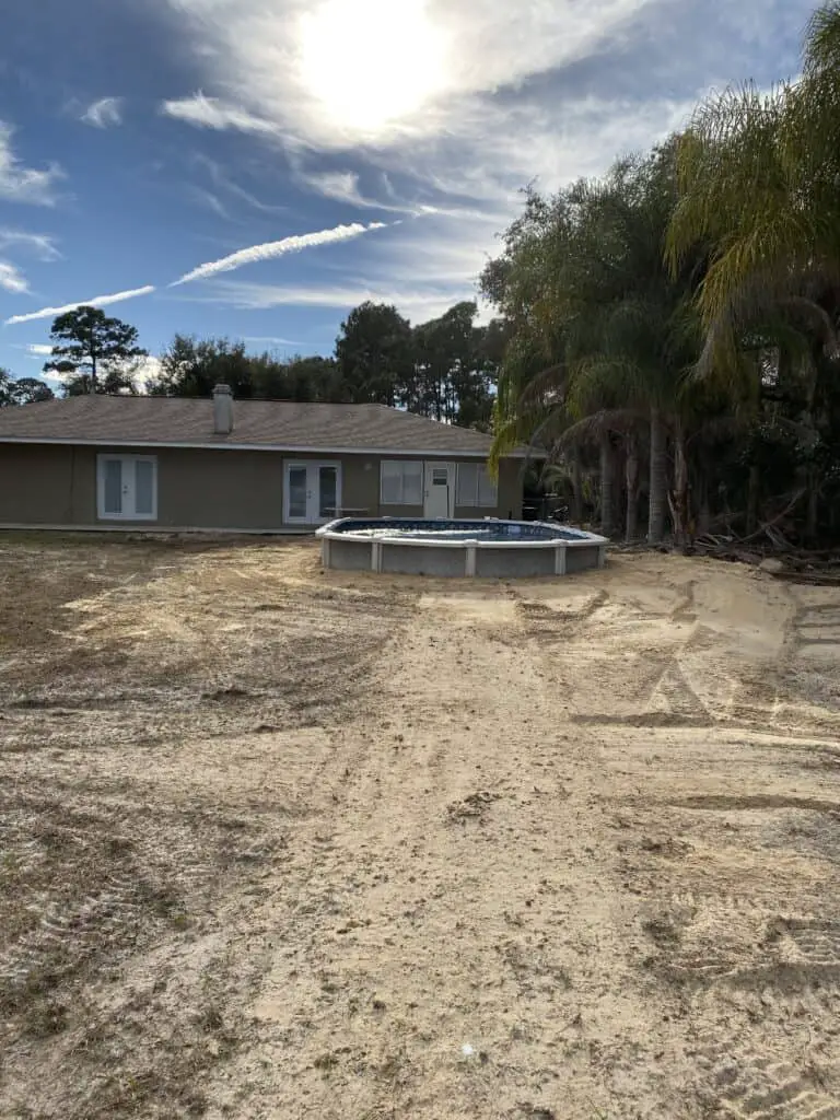 15x30 oval above ground pool partially buried and backfilled in yard with palm trees
