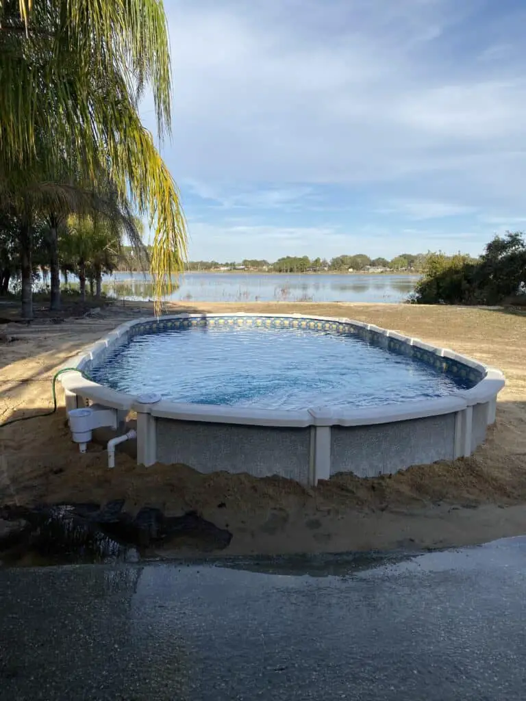 15x30 oval above ground swimming pool in yard with a lake behind it