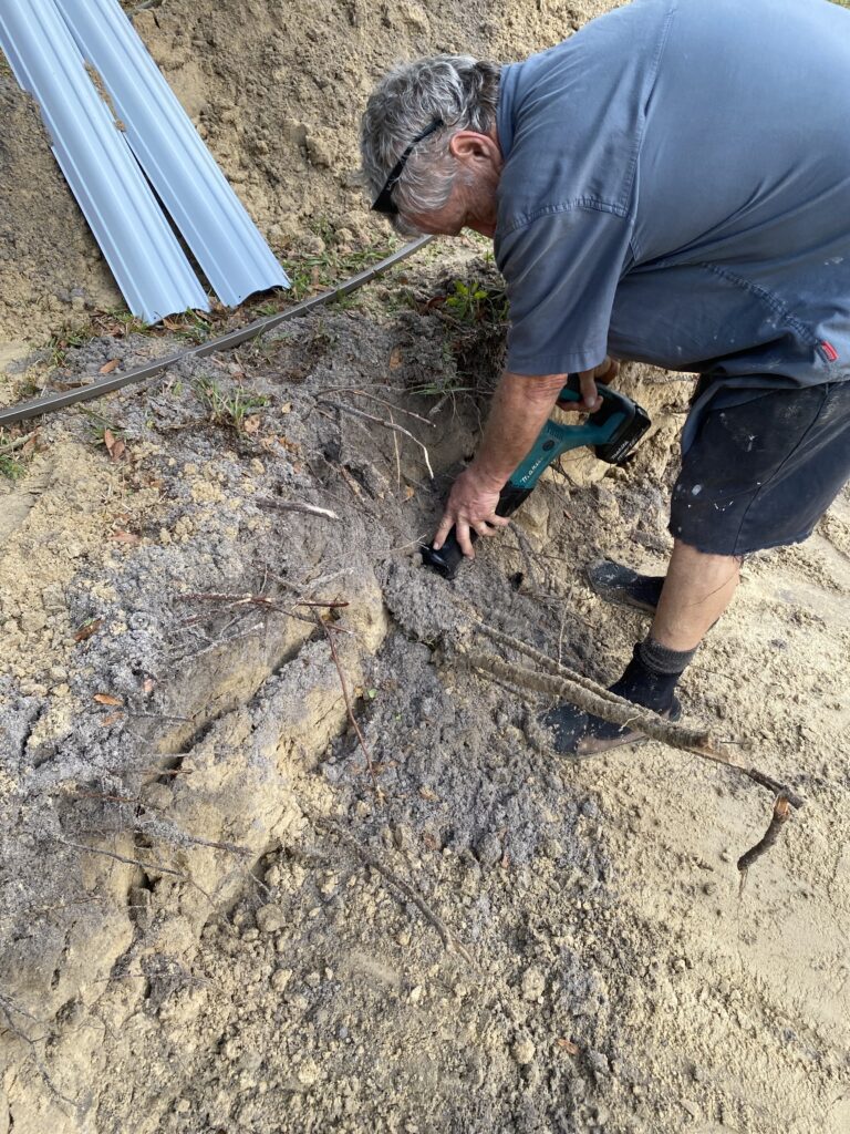 Guy cutting tree roots from an above ground pool semi inground install site using a Sawzall